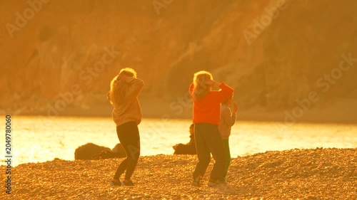 Beach dancing sunset Three young friends enjoy a playful dance on a rocky shore during a beautiful golden sunset by the sea