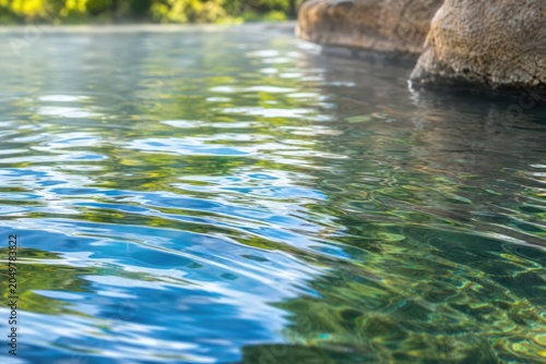Tranquil thermal hot spring water rippling gently near rustic stone border in peaceful outdoor spa resort with steam rising under soft sunlight, close-up view