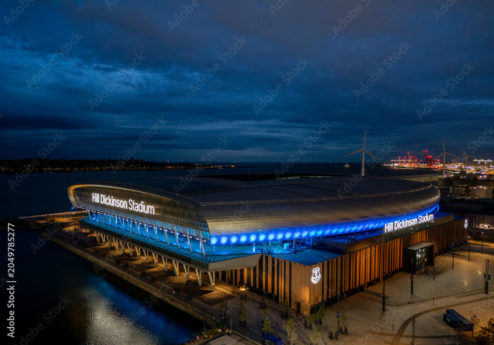 Naklejka premium Hill Dickinson Stadium in Liverpool, Merseyside, England at night. Modern football stadium illuminated after dark on the River Mersey waterfront, aerial view of a major sporting landmark.