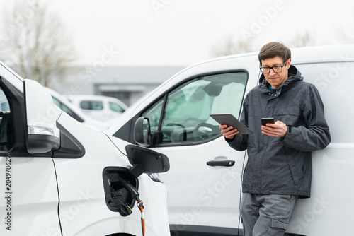 Fleet manager with digital tablet and smartphone supervising rows of white electric delivery vans