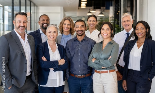 Diverse team of professionals stands together and smiles confidently at the camera in a modern office hallway.