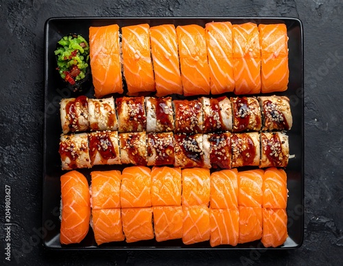 A black tray filled with assorted sushi rolls and sliced salmon sashimi