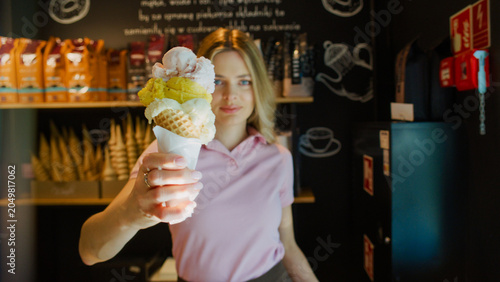 Woman working in an ice cream shop offering a large cone of sweet ice cream to the camera. Selective focus