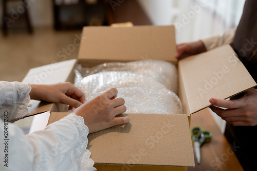 Small business owners packing fragile items with bubble wrap inside cardboard box during e-commerce shipping preparation and logistics fulfillment workflow