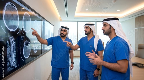 Arab doctors in blue scrubs analyzing brain MRI scans on digital screen in modern medical facility
