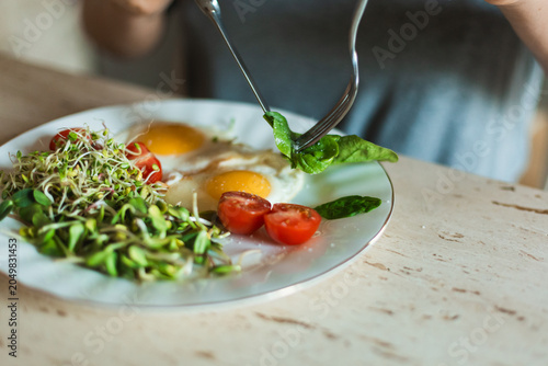 Foto A close up of a person using a fork to pick up fresh green spinach leaves from a plate with fried eggs and microgreens