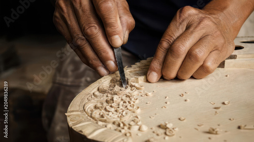 Hands meticulously carving intricate designs into light wood surface.