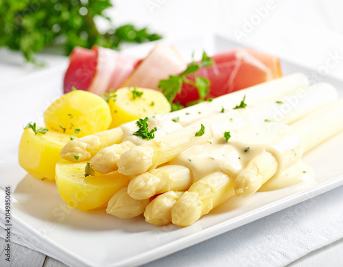 White asparagus with creamy sauce, potatoes and prosciutto, white plate, closeup. AI