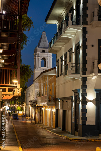 Illuminated street in Panama city's casco viejo with traditional colonial buildings, a prominent san Jose church steeple, and evening activity creating a vibrant urban atmosphere - stock photo