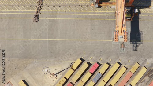 Terminal tractor maneuvering a semi-trailer chassis across a paved container yard. With rows of shipping containers and the shadow of a large gantry crane visible from a top-down aerial perspective