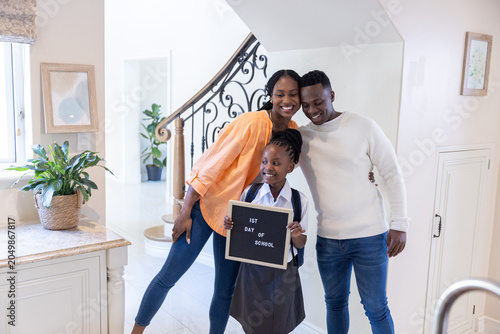 Fotografía African American family posing in foyer, schoolgirl in grey uniform holding 1ST