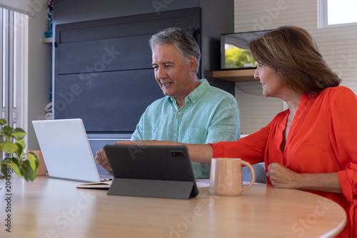 Foto Senior couple collaborating at wooden dining table in home, pointing at silver l