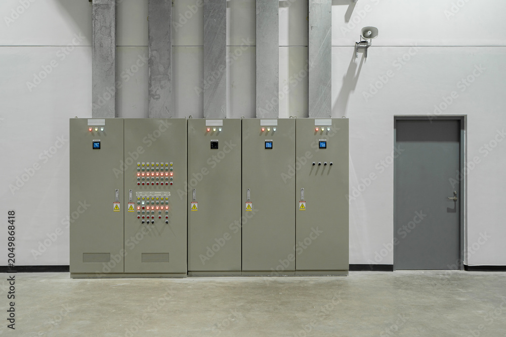 Fototapeta premium Modern industrial electrical control panel with switchgear, indicator lights, and grey door in a clean utility room.