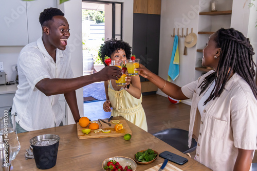 African American parents with child toasting at kitchen island raising orange juice glasses