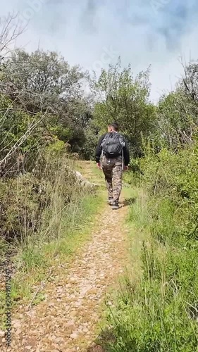 Point of view shot following two men with backpacks walking away on a narrow, rocky trail during a hike in a lush green mountain forest