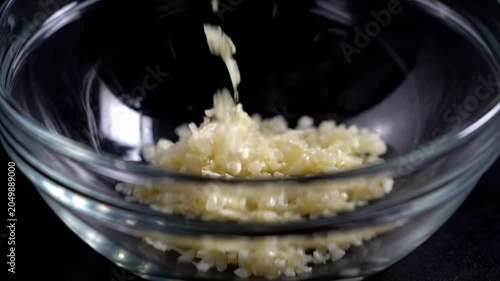 Garlic cloves are washed in a bowl. Chopped garlic falls into a clear glass bowl.