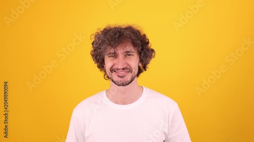 Person smiling and giving a playful wink in a bright yellow studio portrait, creating a friendly upbeat mood.