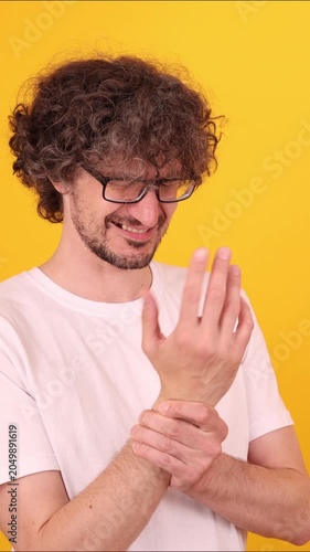 Person holding their wrist with visible discomfort, conveying wrist pain or possible sprain in a bright expressive studio pose.