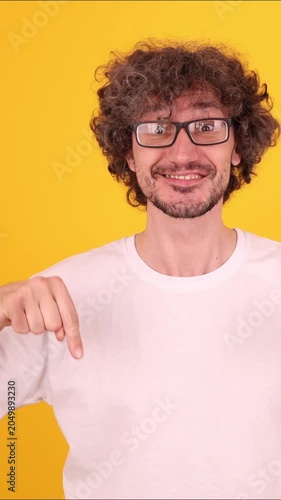 Person looking downward and pointing with an index finger in a bright yellow studio portrait, creating a clear directional gesture.