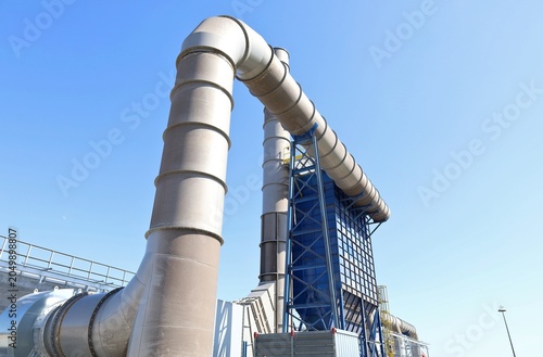 Industrial plant for purification and air pollution control combined with large smoke extraction ducts and an exhaust chimney in the background.
