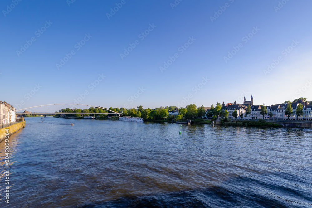 Obraz premium Spring cityscape, Architecture traditional houses and Churches on the riverside under blue sky, The Hoge Brug pedestrian and cycle bridge crossing the Meuse river in Maastricht, Limburg, Netherlands.