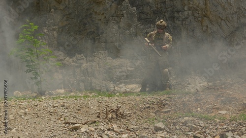 Canvas Print A soldier in full combat gear aims a rifle during a tactical mission in a smoky, rocky quarry, representing modern warfare and special forces operations