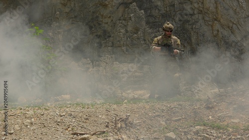 Canvas Print A soldier in full combat gear aims a rifle during a tactical mission in a smoky, rocky quarry, representing modern warfare and special forces operations