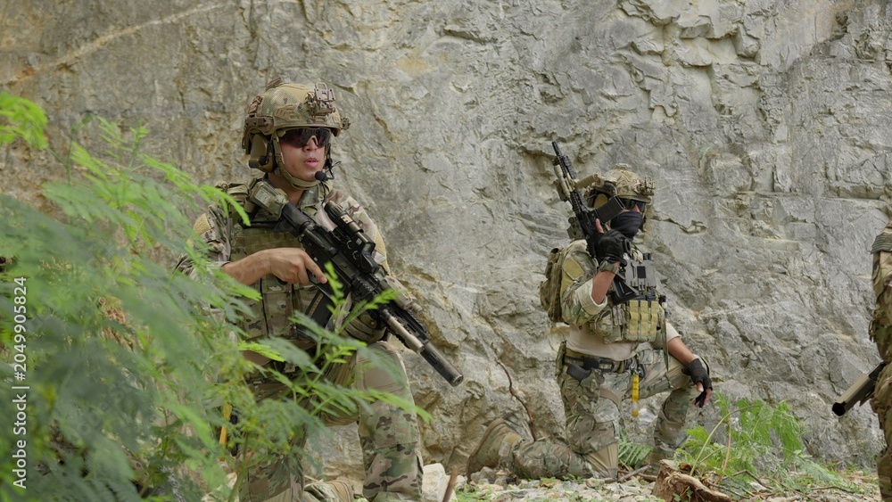 Obraz premium Special forces soldiers on patrol cautiously advance through rocky terrain, conducting a covert reconnaissance mission with tactical gear and assault rifles.