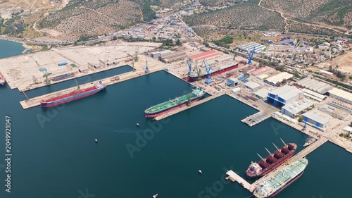 Expansive aerial perspective of a major industrial shipyard with several large cargo ships and oil tankers undergoing maintenance and repair in dry docks and at quayside berths