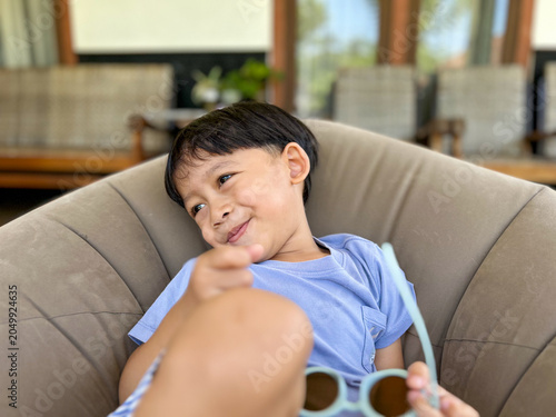 Bild auf Leinwand happy little boy relaxing on a bean bag chair and holding sunglasses indor
