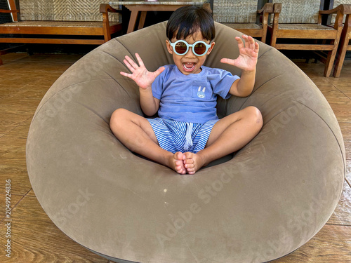 Bild auf Leinwand happy little boy relaxing on a bean bag chair and holding sunglasses indor and l