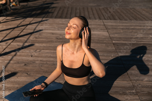 Принти на полотні Woman enjoys music while exercising outdoors during morning sunlight