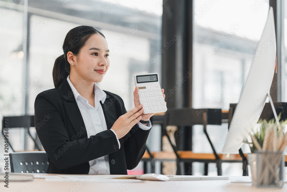 Obraz premium Businesswoman holding a calculator while working at her desk in a modern office