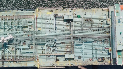 High aerial view showing the intricate pipeline system on the deck of a massive crude oil tanker ship slowly moving through the ocean, highlighting global logistics and energy transportation