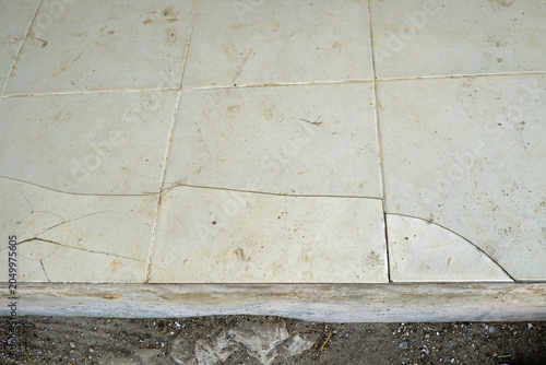 фотографія Light-colored, soiled ceramic floor tiles with prominent, spiderweb-like cracks