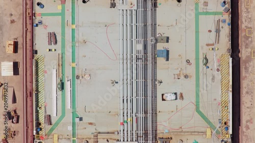 Overhead drone footage capturing the intricate details of a massive vessel's deck, pipelines, and hull structure during its assembly process in a shipyard's dry dock facility