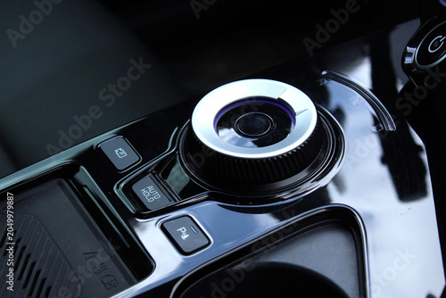 Close-up of rotary gear selector in modern electric vehicle, featuring premium glossy surfaces, electronic parking controls, and advanced driver interface technology. Contemporary automotive interior 