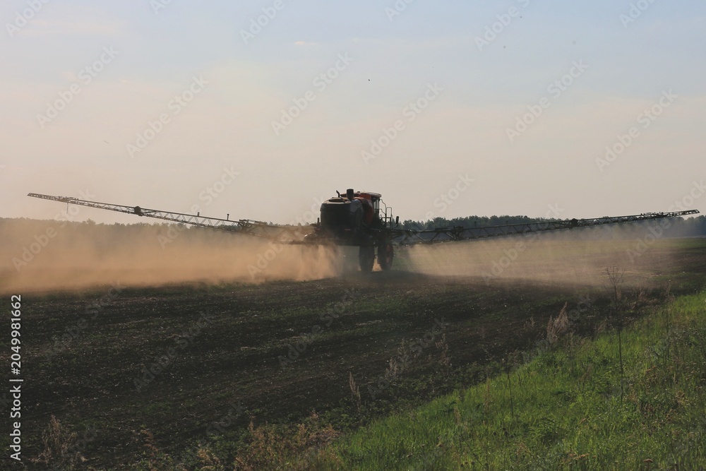 Fototapeta premium agricultural machinery fertilizes a farm field with crops