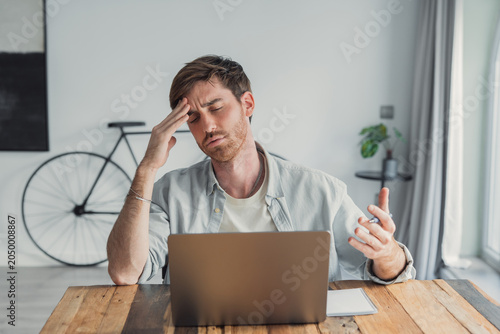 Tableau sur toile Young man experiencing stress, migraine, or headache while working on a laptop a