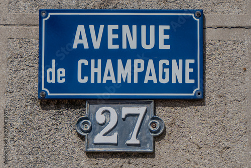 Epernay, France, May 23, 2026. A traditional blue enamel street sign reading Avenue de Champagne above a vintage metal plate showing house number 27, mounted on a grey stone textured wall.
