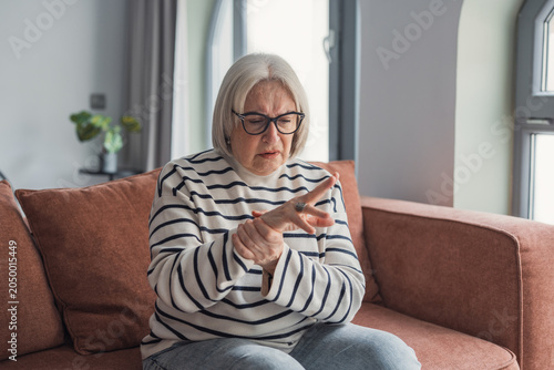 Tableau sur toile Senior woman is experiencing discomfort and pain in her wrist and hand, massagin