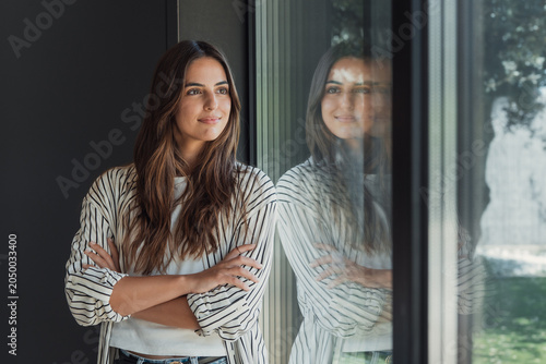 Obraz na płótnie Woman standing with crossed arms, looking out a large window and reflecting on h