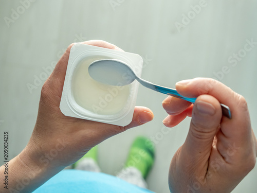 Woman stirring plain yogurt in container, healthy breakfast top down