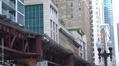 Elevated train tracks curve through dense Chicago downtown architecture. Skyscrapers and historic buildings create layered urban cityscape.