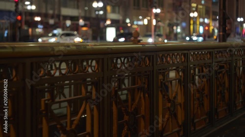 Chicago street scene at night with decorative metal bridge railing and blurred city lights in the background. Urban infrastructure and traffic create a warm illuminated evening atmosphere.