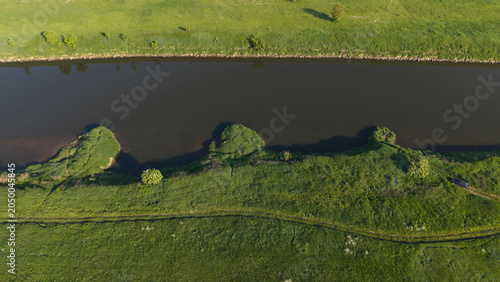 Slika na platnu Top down aerial view of a green riverbank and dark river water