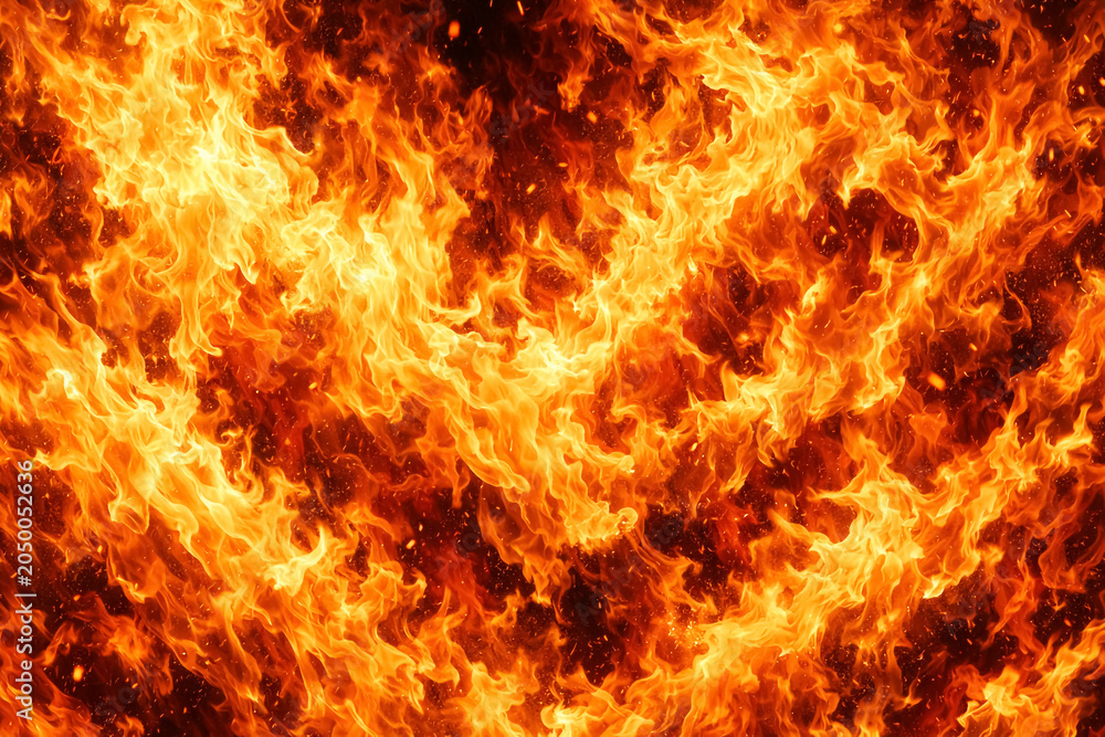 Fototapeta premium Firestorm of orange flames roars with chaotic energy as brilliant sparks fly through the darkness to illuminate the scene with a powerful display of raw combustion and intense thermal radiation.