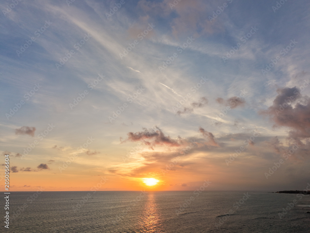Fototapeta premium Aerial view of a beautiful golden sunset over the calm ocean horizon with clouds