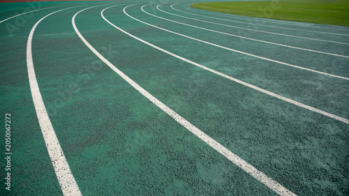 A green running track with white lanes curving around an outdoor athletic field at a sports facility
