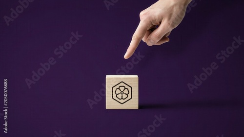 A hand points to a wooden block with a symbol on it against a dark purple background.